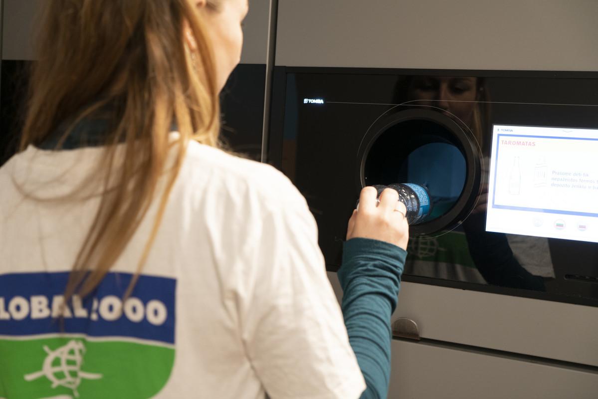 Frau mit GLOBAL 2000 T-Shirt legt eine Plastikflasche in einen Pfandflaschen-Automaten