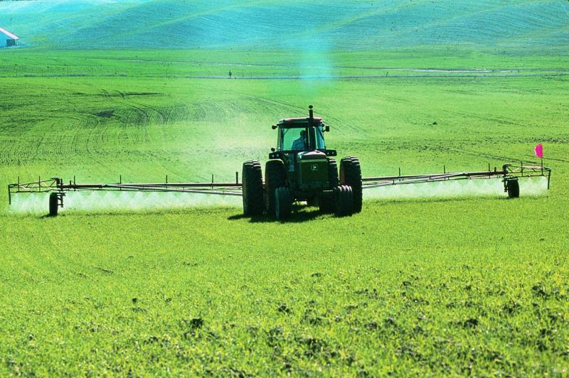 Ein Traktor versprüht Pestozide auf einem grünen Feld