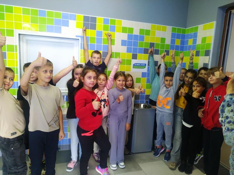 Eine Gruppe Kinder steht vor einer Wasseraufbereitungsanlage und wirft die Hände vor Freude hoch