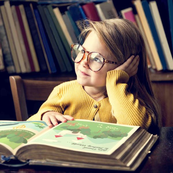 Kind mit Brille und Buch schaut verträumt