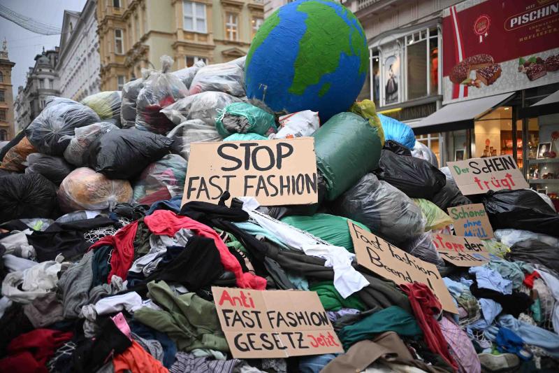 Kleiderhaufen mit Erdkugel auf Spitze und Schildern mit Stopp Fast Fashion