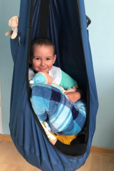 Ukrainisches lächelndes Kind mit Puppe und Spielzeug in Hängematte