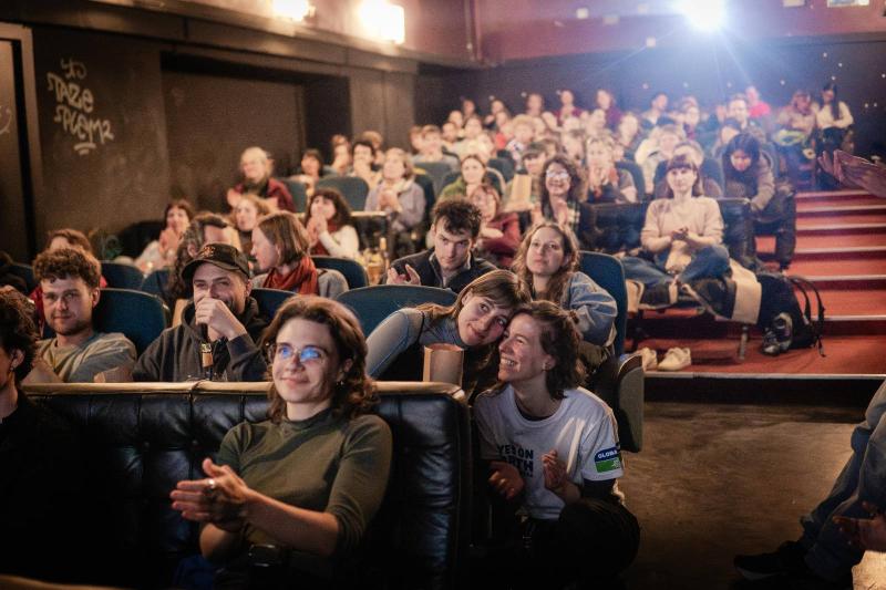 Kinosaal Blick von vorne auf das Publikum, der Saal ist beleuchtet und die lächelnden Menschen sind sichtbar