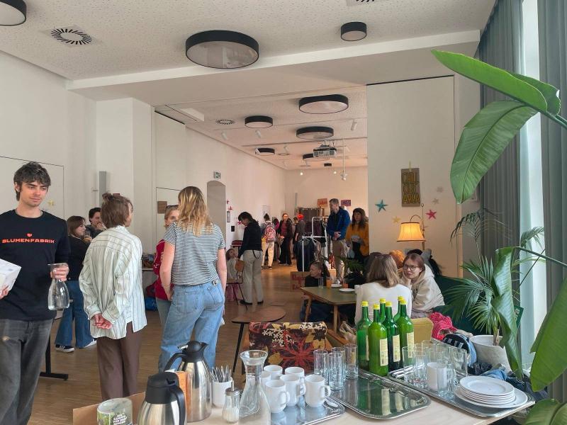 KLeidertauschparty in der Blumenfabrik, man sieht Menschen in einem Saal und ein Buffet mit Gläsern, Theromskannen und Flaschen