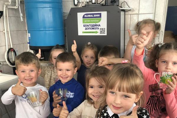 Kinder vor Wasseraufbereitung lachend und mit Daumen hoch