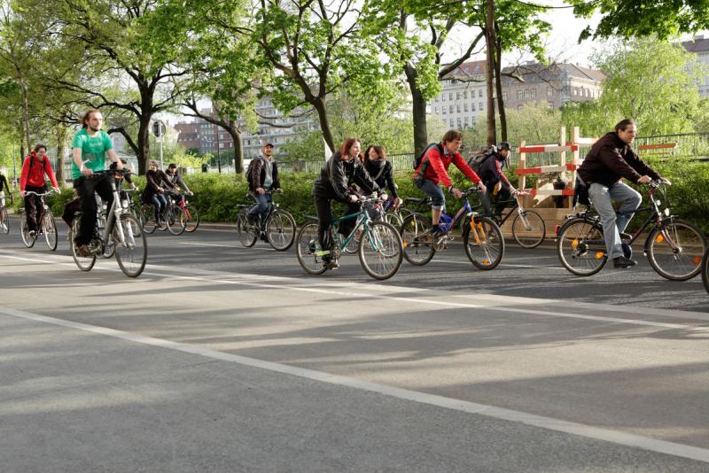 Viele Menschen auf Fahrrädern fahren durch Wien auf Straße und an grünen Bäumen vorbei