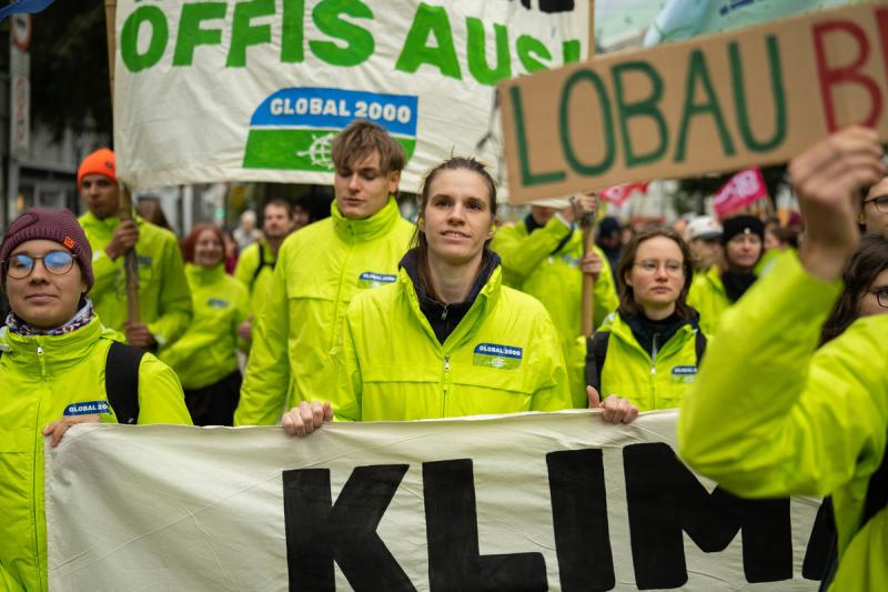 Hannah Keller und demonstrierende Menschen in grünen Jacken halten Schilder hoch mit der Aufschrift Lobau bleibt und Öffis ausbauen