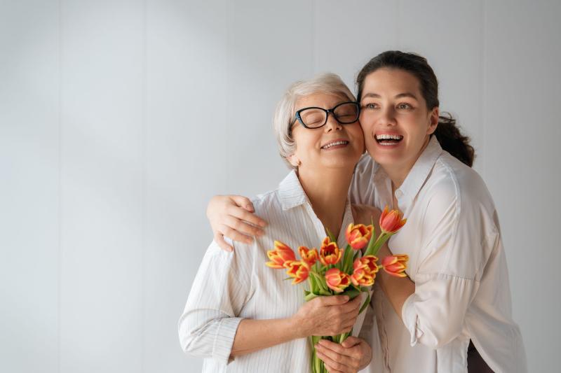 Zwei Frauen umarmen sich, eine hält einen Blumenstrauß mit Tulpen - Muttertag!