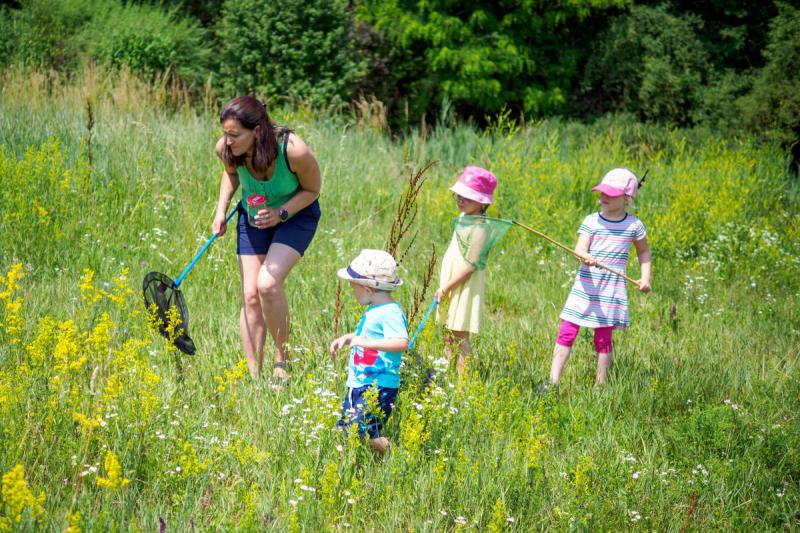 Frau mit Kescher und drei Kinder mit Hüten in einer blühenden Wiese