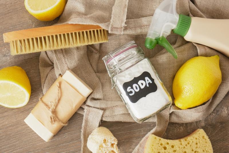 Bürste, Glasbehälter mit Aufschrift 'SODA', Seifenstück, Sprühflasche, Zitronen und Schwämme auf Stoff und Holztisch - Beispiele für chemiekalienfreier Haushalt