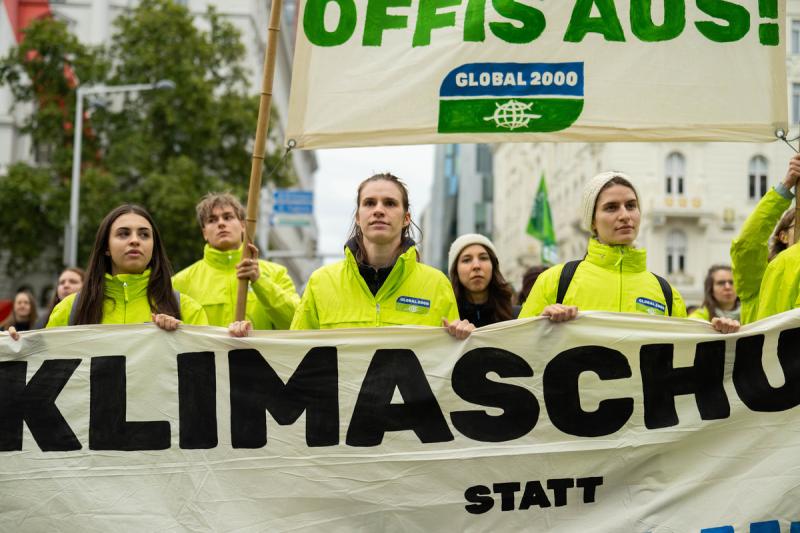 Demo für Umweltschutz: Gruppe von Menschen in gelben GLOBAL 2000-Jacken hält ein Banner mit der Aufschrift 'KLIMASCHU' bei einer Demonstration