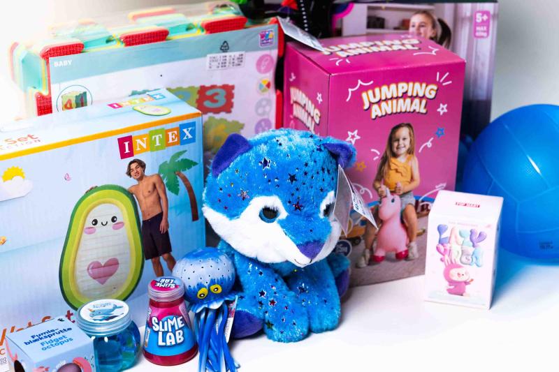 Verschiedene bunte Spielzeuge, darunter ein blaues Plüschkätzchen mit Sternen, ein aufblasbares Planschbecken mit Pinguinmotiv, ein rosa hüpfendes Tier auf einer Verpackung mit der Aufschrift 'JUMPING ANIMAL' und mehrere kleine Spielzeugbehälter und -flaschen