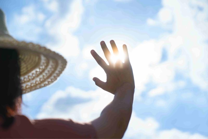 Hand einer Person vor strahlend blauem Himmel mit Sonne, die durch die Finger scheint