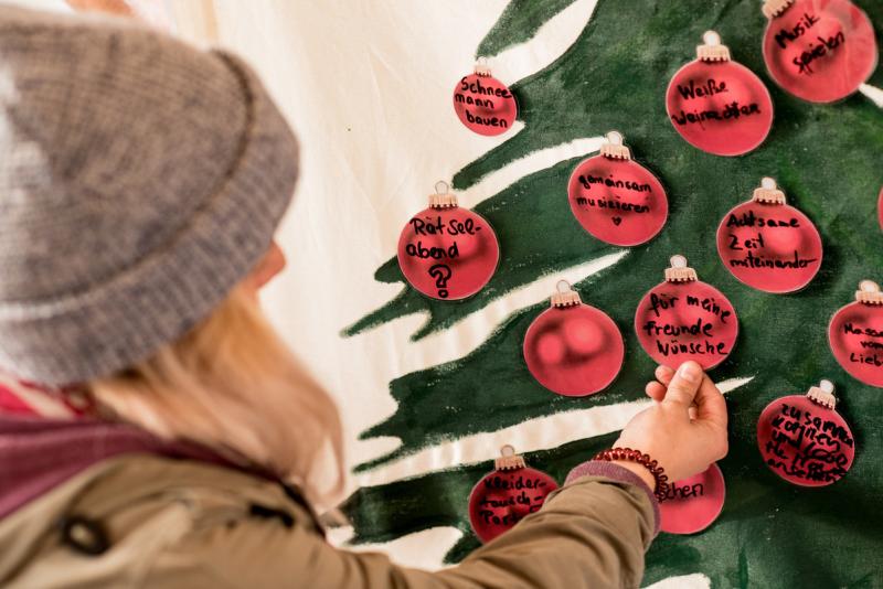 Frau mit blonden Haaren und Mütze berührt Adventskalender in Christbaumform