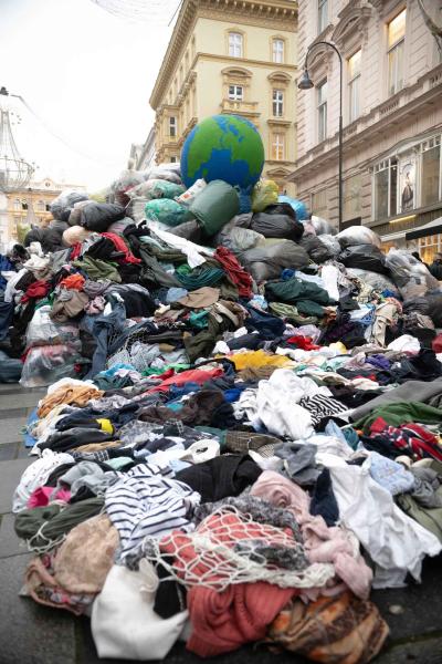 Großer Haufen ausgebrauchter Kleidung auf einer Straße mit einem großen Globus als Symbol im Hintergrund bei einer Aktion von GLOBAL 2000