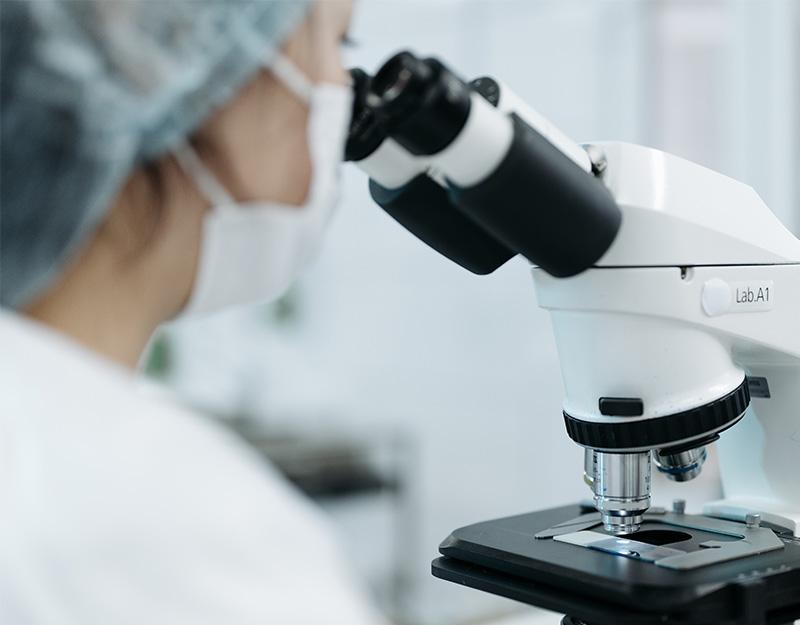 Frau schaut im Labor durch ein Mikroskop