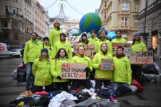 GLOBAL 2000 Mirarbeiter:innen mit grünen Jacken vor Kleiderhaufen
