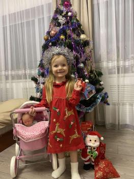 Lächelndes Mädchen mit Puppenwagen und Geschenken vor Weihnachtsbaum