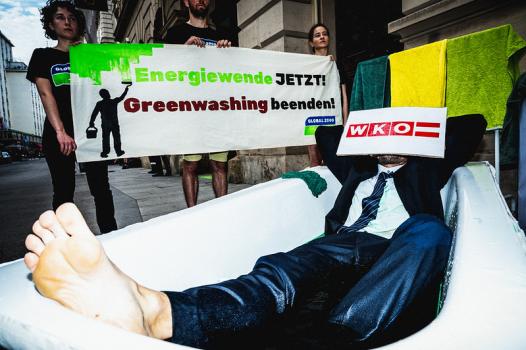 Aktivist:innen von GLOBAL 2000 und WKÖ bei einer Aktion mit Banner „Energiewende JETZT! Greenwashing beenden!“ und einer Person in einem Badewannen-Kostüm.