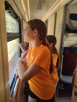 Zwei Mädchen in orangefarbenen T-Shirts stehen im Zug und schauen aus dem Fenster