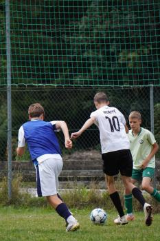 Drei Jungen spielen Fußball vor einem Tor mit grünem Netz auf einem Rasenplatz