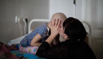 Frau küsst ukrainisches Kind auf Krankenbett