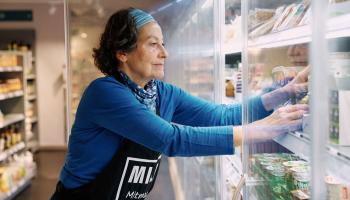 Frau mit MILA Schürze räumt Waren ins Tiefkühlregal