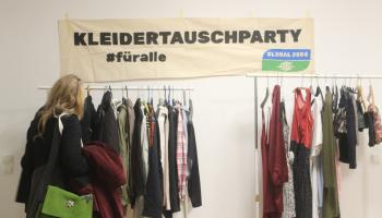 KLeidertauschparty Ständer stehen vor einem Schild und Frau betrachtet Kleidung