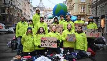 Aktivist:innen von GLOBAL 2000 protestieren mit Kleidungsberg und Erdball für Anti-Fast-Fashion-Gesetz