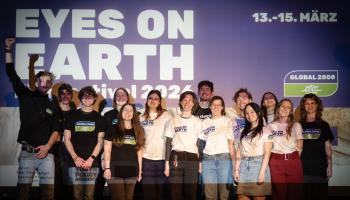 Gruppe von Menschen steht vor einer Wand mit dem Schriftzug 'EYES ON EARTH festival 2023' und dem Datum '13.-15. MÄRZ'