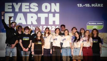 Team*Aktiv steht vor einer Wand mit dem Schriftzug 'EYES ON EARTH Festival 