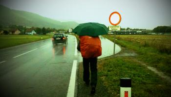 Wanderer mit rotem Rucksack und grünem Regenschirm an Landstraße