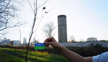 Hand hält GLOBAL 2000 Sticker in die Kamera vor einem Atomkraftwerk