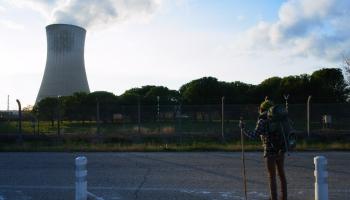 Wanderer mit Wanderstock steht auf Straße und blickt auf Atomkraftwerk