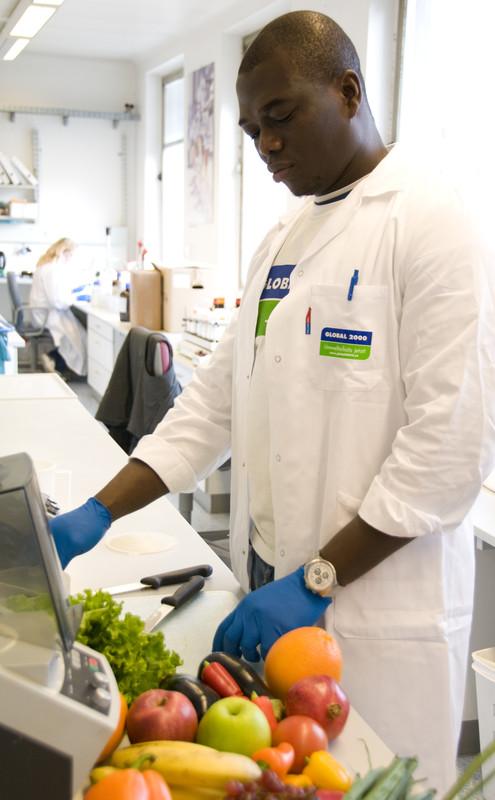 Laté Lawson steht mit einem weißen Kittel in einem Labor und untersucht Obst