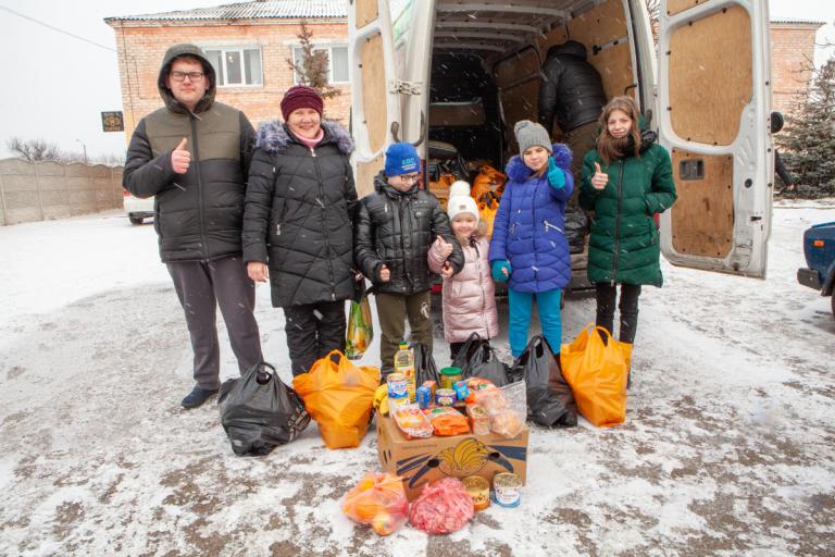 Eine ukrainische Famile steht vor einem Lieferwagen im Schnee und freuen sich über die Hilfsspenden, die vor ihnen stehen