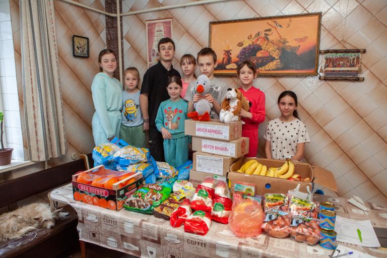Eine Familie posiert mit den erhaltenen Hilfspenden in ihrem Wohnzimmer