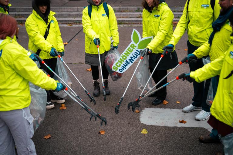 GLOBAL 2000-Freiwillige in grünen Jacken stehen im Kreis und werden Müllsammeln