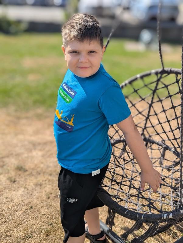 Junge steht neben einem runden Netzschaukelkorb auf einem Spielplatz und schaut in die Kamera