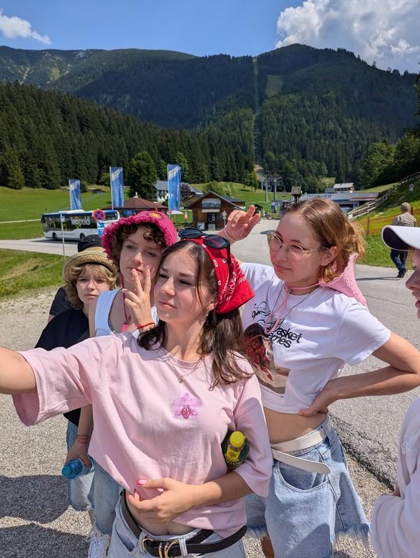Gruppe junger Menschen vor Berglandschaft macht Selfie, eine trägt rosa T-Shirt und rotes Halstuch