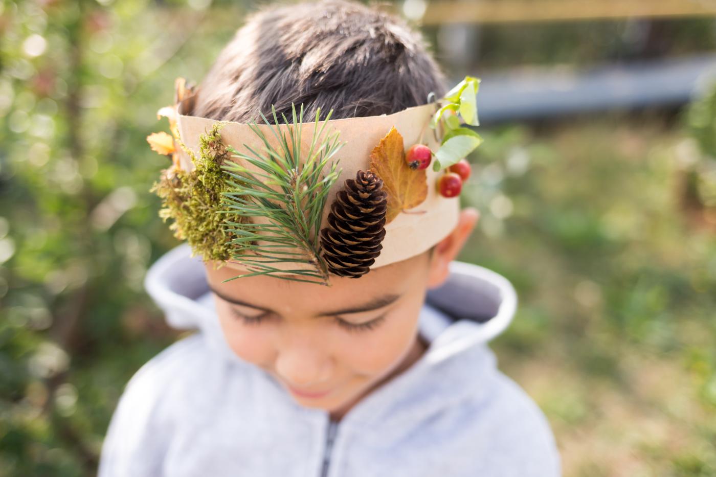 Kind mit einem Stirnband mit Zweigen, Zapfen und Blättern