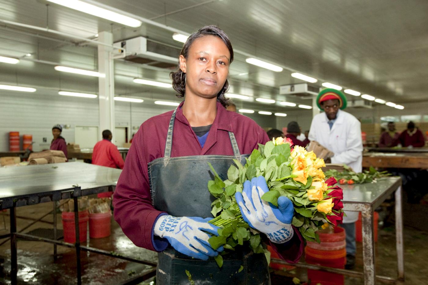 Arbeiterin hält Strauß mit Rosen in Fabrikshalle in der Hand und schaut in die Kamera