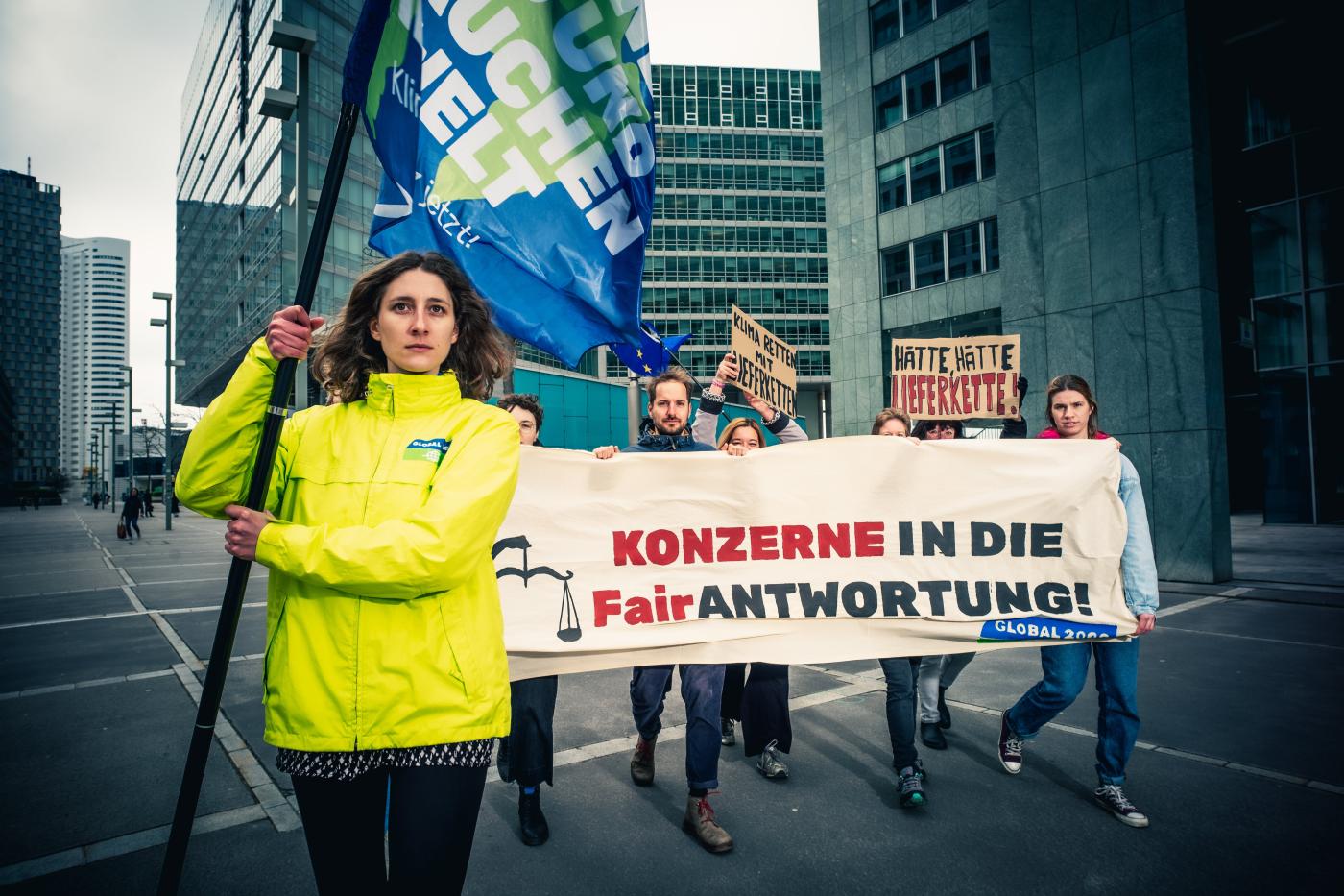 Anna Leitner steht im Vordergrund mit GLOBAL 2000 Fahne in der Hand. Im Hintergrund sind Aktivist:innen zu sehen, die einen Banner in der Hand halten. 