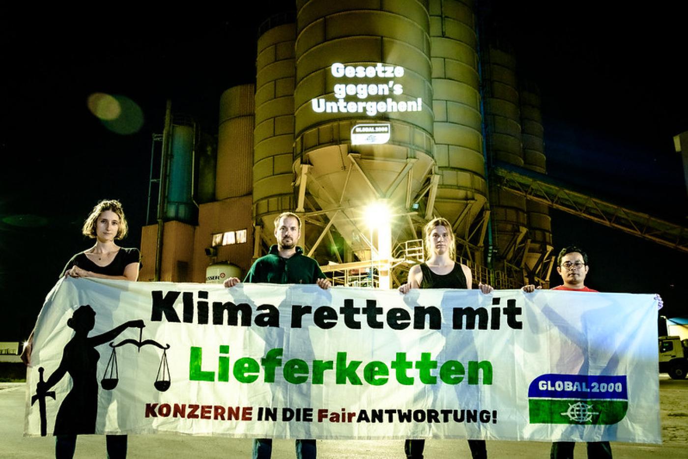 Aktivist:innen stehen vor der Firma Holcim und halten ein großes Banner in die Kamera. Darauf steht "Klima retten mit Lieferketten"