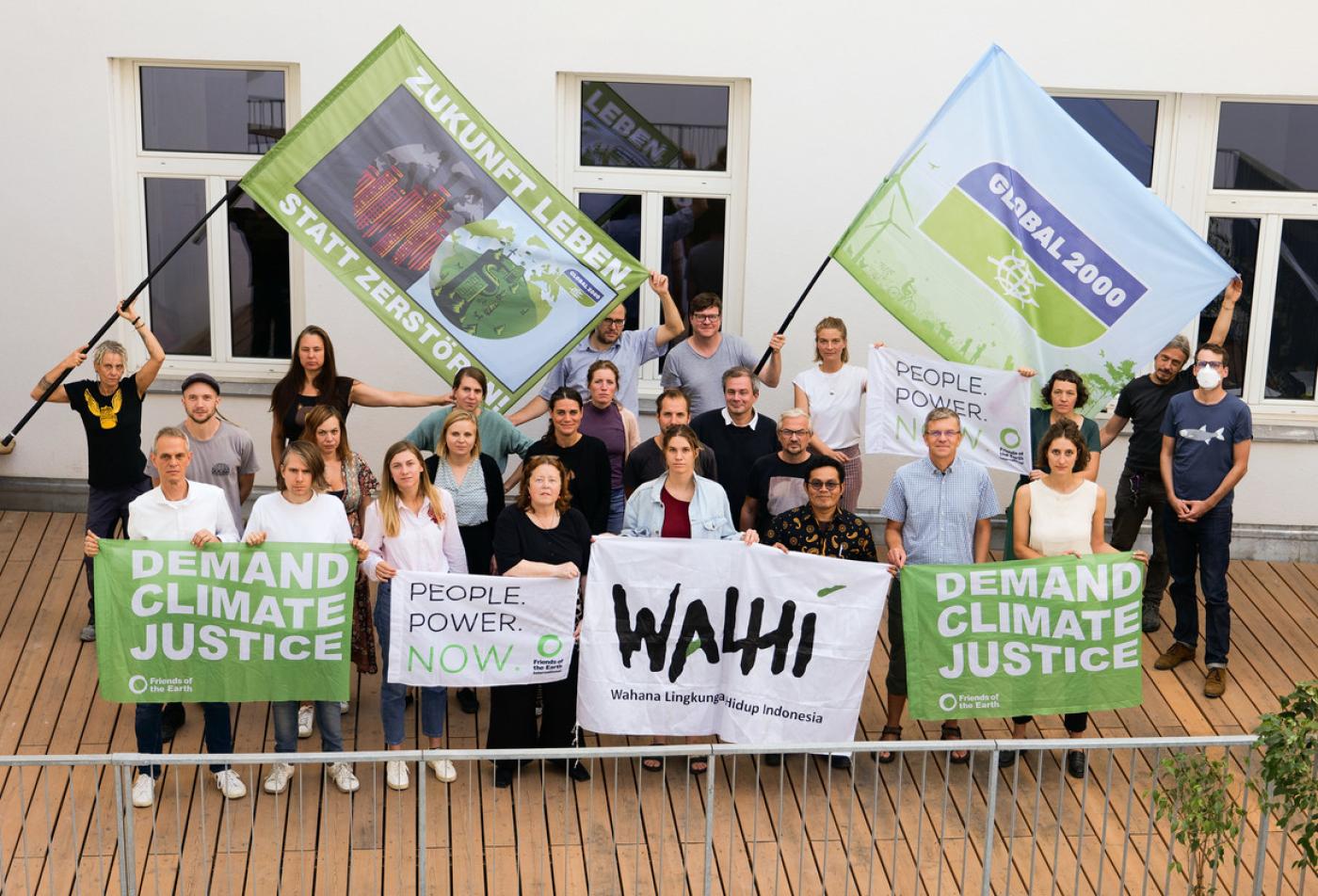 Gruppenfoto von GLOBAL 2000 Mitarbeiter:innen mit Parid und Yvan - dabei werden Fahen und Banner in die Kamera gehalten. Darauf finden sich Slogans wie "Demand Climate Justice" und "Zukunft leben statt zerstören"