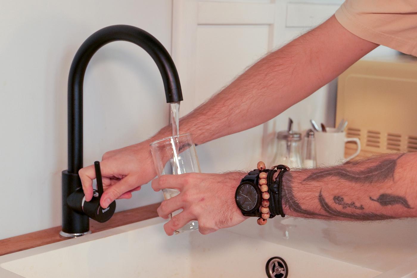 Eine Person lässt Wasser in ihr Wasserglas über den Wasserhahn fließen