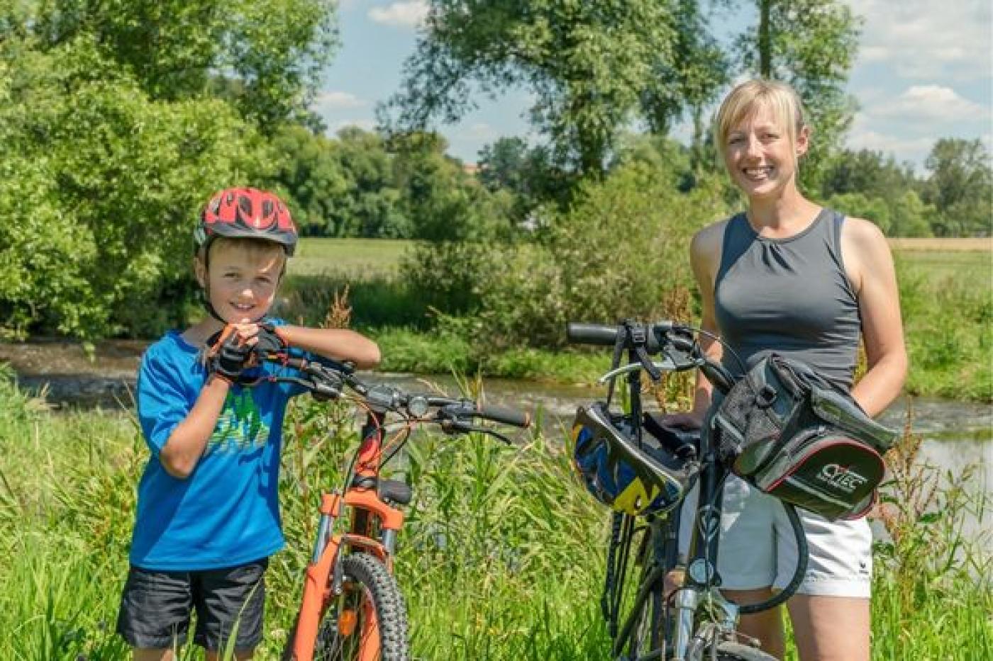 Eine blonde Frau und ein kleiner Junge schieben ihre Fahrräder durch die Natur