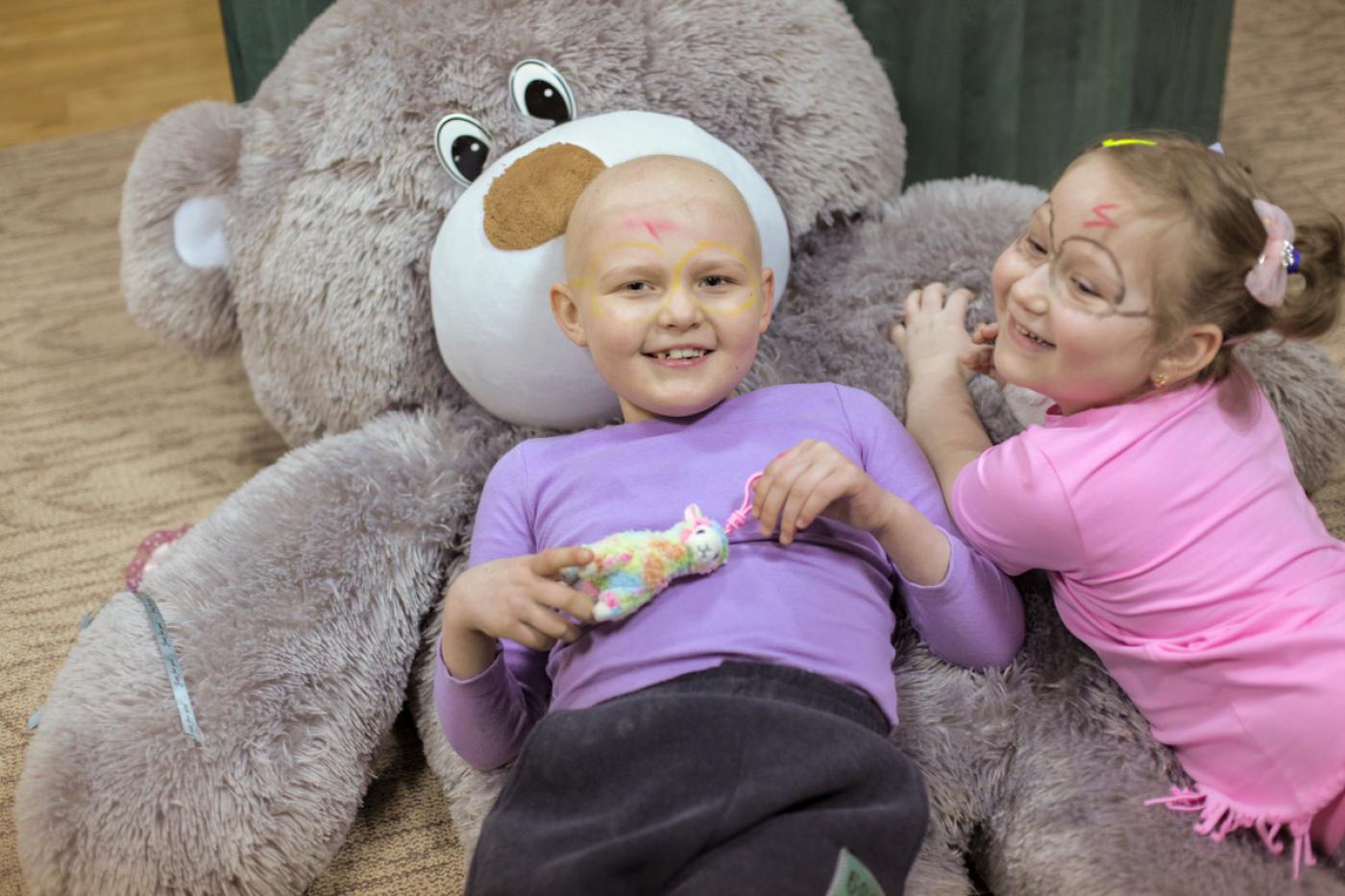 Zwei Kinder liegen auf einem großen Stoffbären und lachen in die Kamera