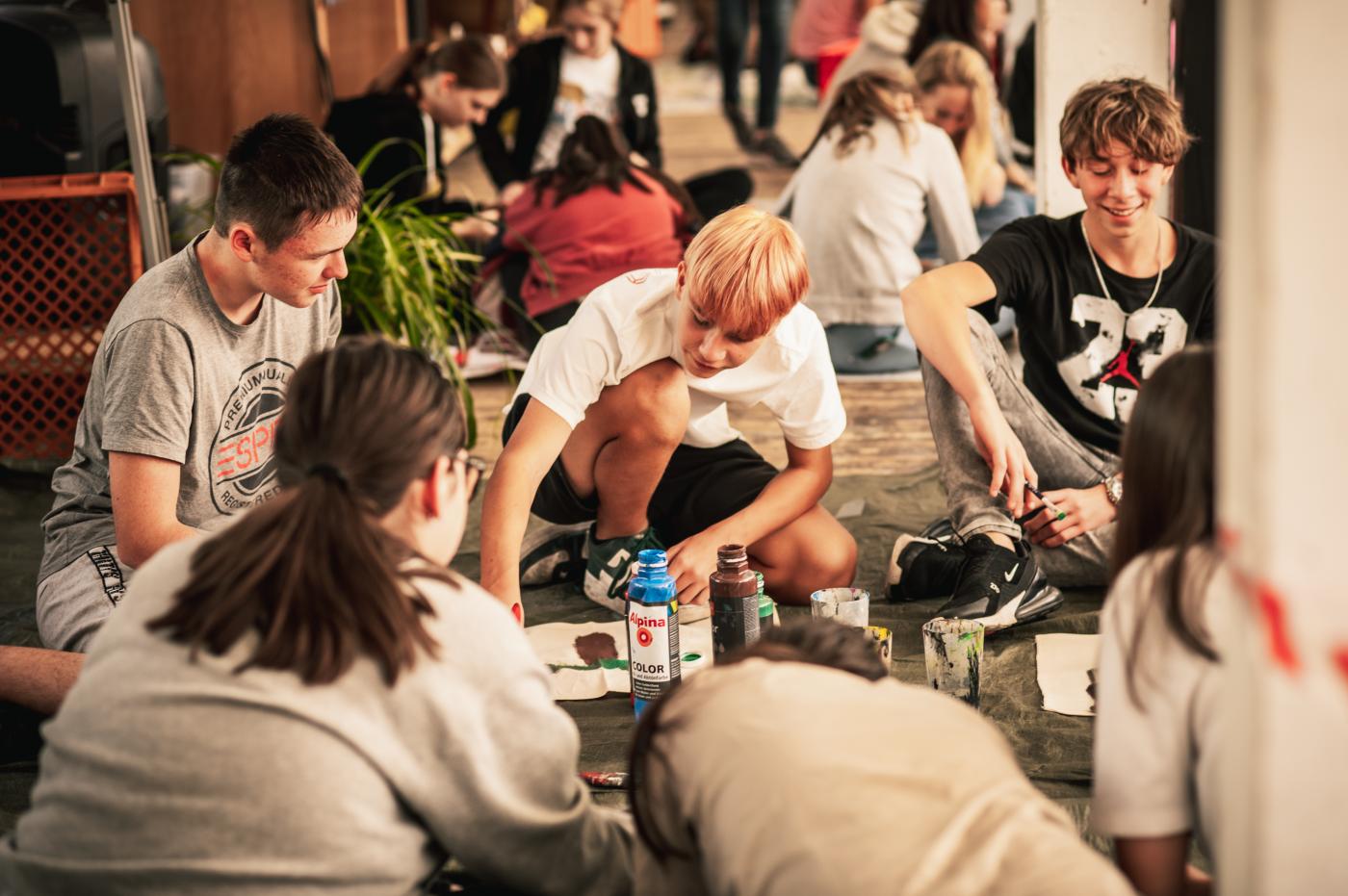 Jugendliche sitzen am Boden und malen ein Plakat