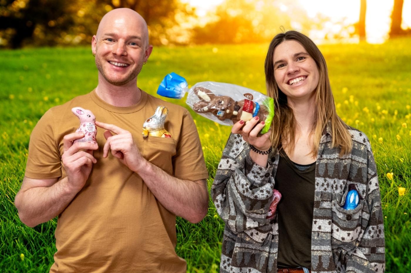 Ein junger Mann und eine junge Frau halten Schoko-Osterhasen in die Kamera und lachen
